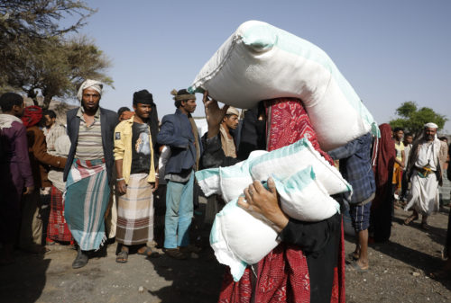 Jemenissä nainen kantaa avustuspakettia. Ihmisiä taustalla odottelemassa.