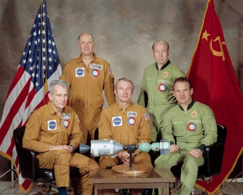 Kolme astronauttia ja kaksi kosmonauttia yhteiskuvassa Yhdysvaltojen ja Neuvostoliiton lippujen edessä.