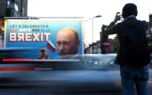 Ohikulkija kuvaa katukylttiä, jossa Putin iskee silmää ja tekstissä juhlitaan brexitiä.