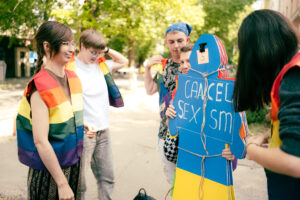Nuoria on kerääntynyt Ukrainan-lipun väreihin maalatun siluetin ympärille. Siluetissa lukee "Cancel sexism".